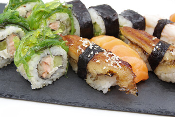 Japanese sushi food on a black tray: sushi rolls, salmon nigiri, shrimp nigiri, unagi nigiri