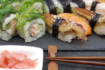 Japanese sushi food on a black tray, served with ginger, soy sauce and seaweed salad. Sushi rolls, salmon nigiri, shrimp nigiri, unagi nigiri