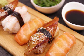 Japanese sushi food on a wooden tray, served with ginger, soy sauce and seaweed salad. Salmon nigiri, shrimp nigiri, unagi nigiri