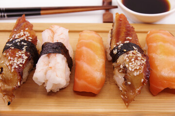 Japanese sushi food on a wooden tray, served with ginger, soy sauce and seaweed salad. Sushi rolls, salmon nigiri, shrimp nigiri, unagi nigiri
