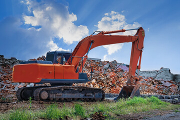 Fototapeta na wymiar An orange excavator stands against the backdrop of a destroyed building and a blue sky.