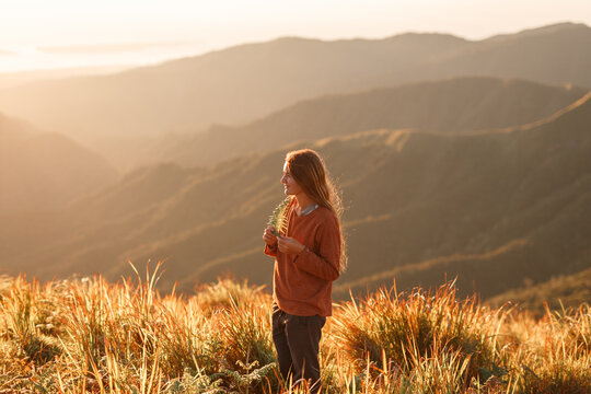 Young woman tourist looks at the sunrise in the mountains in a orange sweater, warm colors