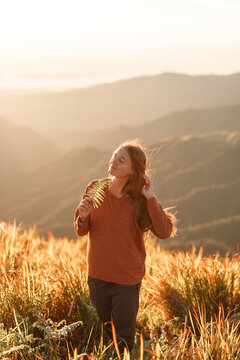 Woman traveler standing on  the top of mountains, welcomes a sun. Sunrise on the meadow, warm orange sunny colors