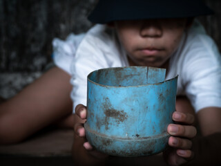 Child or poor homeless holding plastic bowl with hungry and asking help food donation from traveler on street at the city. Unidentified homeless child begging on street. Shelter concept.
