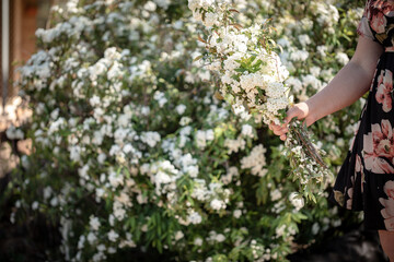 Woman wearing floral dress holding bunch of white flowers in beautiful cottage garden