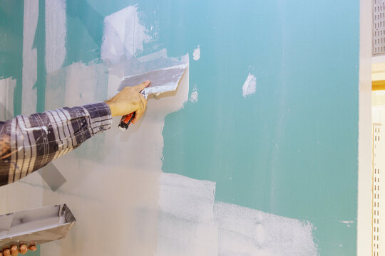 Man aligning a wall with spatula working with putty and spatula wall