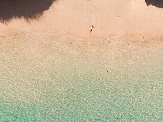 Young woman in a bikini lying on the back on the white sand near the waves of blue sea. Top view, aerial shooting