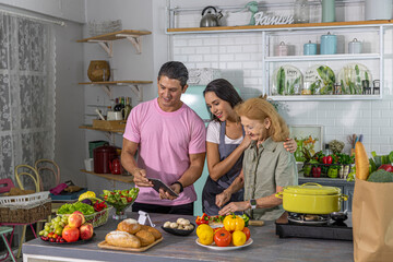 Young couple working with grand mom to take online cooking course and prepare meal at home. Happy family is cooking breakfast with healthy food together