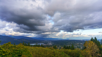 Cloudy Fraser Valley with views of Port Moody at Burrard Inlet, trees in foreground and distant mountains