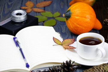 A white cup of tea coffee on a wooden background. Ripe pumpkin. Cones and leaves on a wooden table. Open notebook.
