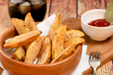 Rustic fries potatoes with herbs in a ceramic bowl on a wooden board with barbecue sauce on wooden table