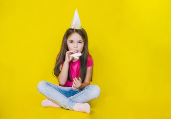 Little cute happy girl looking at the camera in a festive hat on a yellow background.The child's birthday.