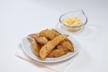 Rustic or Country Style Herb Fries potatoes on a Small white Plate with Herb Mayonnaise on a White Surface