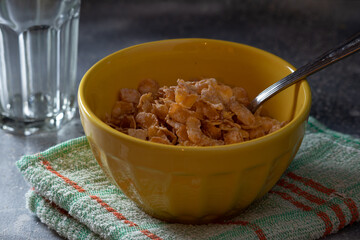 Cornflakes in a yellow bowl on rustic surface or background - Crunchy cereal petals for breakfast