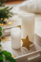 White thick candles and wooden stars on a tray. Light winter interior with Christmas decor and fluffy textiles.