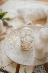 A magic glass snow globe with deer and a garland on the bedside table in a light interior.