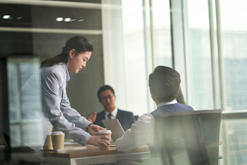 young asian intern serving coffee to senior management meeting in conference room