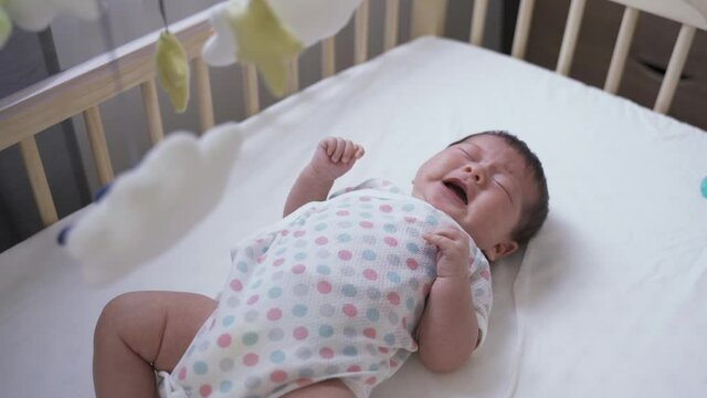 high angle shot upset newborn infant lying alone in the baby bed is crying and screaming loudly in the home nursery room.