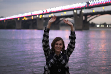 Portrait of a happy young woman in front of the bridge, hands to the sky
