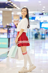 Positive Asian schoolgirl holding paper-bags when standing in mall