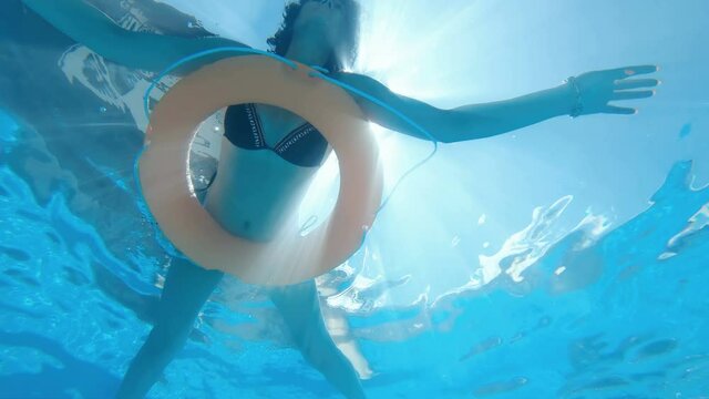 Brunette woman in sunglasses enjoys the sun swimming in the pool lying on rubber ring. Underwater slow motion view