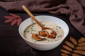 Bowl of mushroom cream soup on a dark wooden background with autumn leaves, close up
