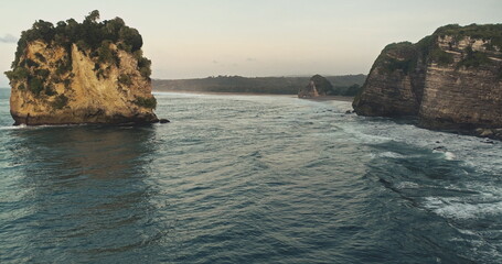 Slow motion seascape with rocks and sand coast aerial view. Ocean waves slowly run to cliff shore. Nobody nature scape at cloudy summer day. Sumba island scenic of sea bay at dramatic drone shot