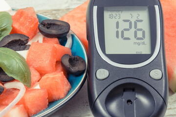 Glucometer for checking sugar level and summer salad of watermelon with feta cheese. Healthy food during diabetes containing vitamins and minerals