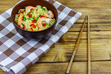 Bowl of instant Chinese noodles with shrimps, green onion and red hot chilli peppers on wooden table