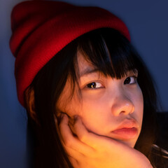 A closeup of an attractive Asian girl wears a red beanie in isolated blue background