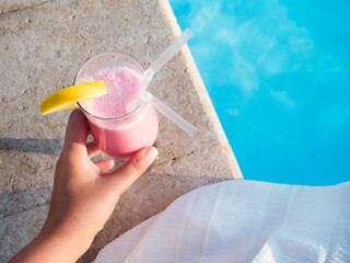 Glass with a beautiful milkshake on the background of the pool. View from above, close-up. Concept of leisure and travel