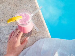 Glass with a beautiful milkshake on the background of the pool. View from above, close-up. Concept of leisure and travel
