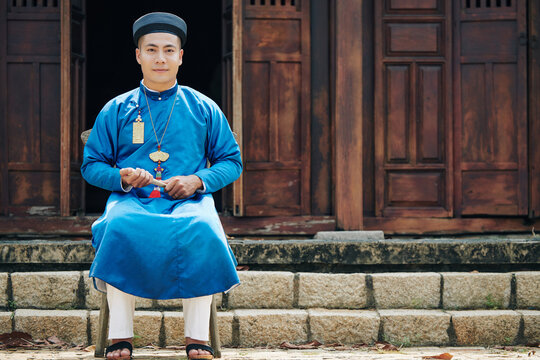 Handsome young man in traditional ao dai dress sitting on stool in front of old temple