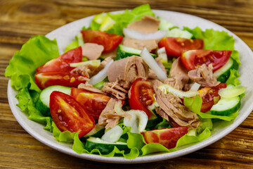 Tasty tuna salad with lettuce and fresh vegetables on wooden table