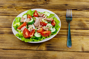 Tasty tuna salad with lettuce and fresh vegetables on wooden table