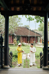 Happy young Asian couple in ao dai dresses walking to temple
