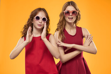 Happy sisters in red dresses on a yellow background are having fun and gesticulating Copy Space