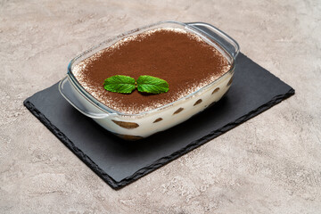 Traditional Italian Tiramisu dessert in glass baking dish on concrete background