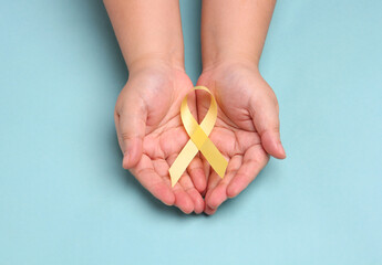 hands holding yellow gold ribbon on blue background , Bone cancer, childhood cancer awareness,...