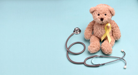 Teddy Bear yellow gold ribbon with stethoscope on blue background , Bone cancer, childhood cancer awareness, World Suicide Prevention Day, Sarcoma Awareness