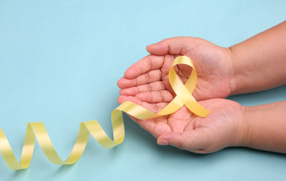 hands holding yellow gold ribbon on blue background , Bone cancer, childhood cancer awareness, World Suicide Prevention Day, Sarcoma Awareness