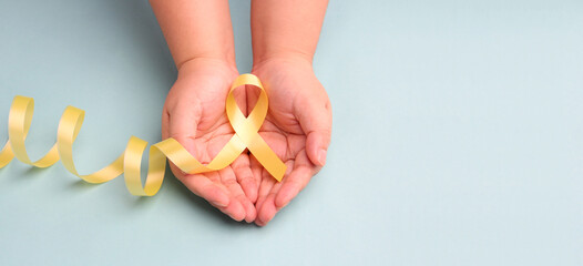 hands holding yellow gold ribbon on blue background , Bone cancer, childhood cancer awareness, World Suicide Prevention Day, Sarcoma Awareness