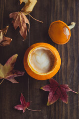 cup of coffee in pumpkin with autumn leaves
