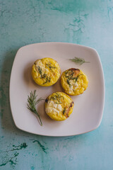 overhead photo of baked egg bites with dill on white plate