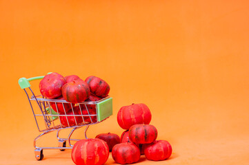 Toy shopping trolley full of mini fake pumpkins. Autumn still life. Bright orange background. Halloween concept