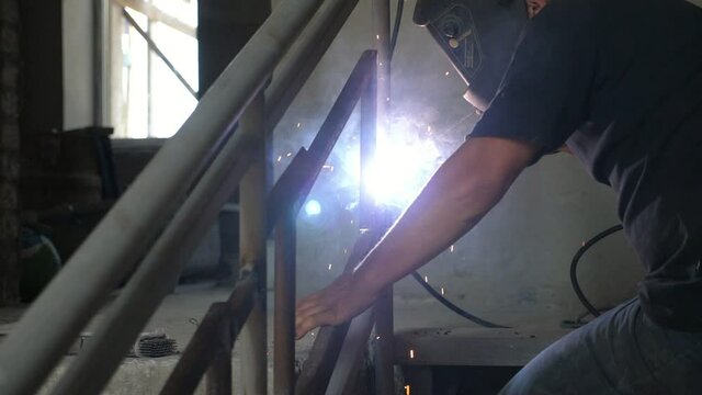 Young worker keeping arc welding device making handrails in a workshop in slo-mo 