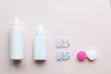 Contact lenses, lens solution and lens containers on a light pink background. Health care concept top view copy space
