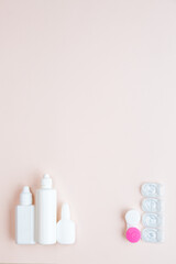 Contact lenses, lens solution and lens containers on a light pink background. Health care concept top view copy space