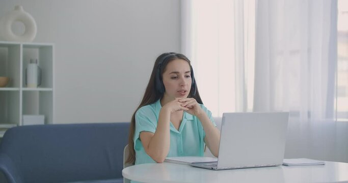 student woman sit at desk at home wear headset talk distantly by video call app and laptop device e-learn language studying with e tutor or classmate do common task remotely, modern tech concept