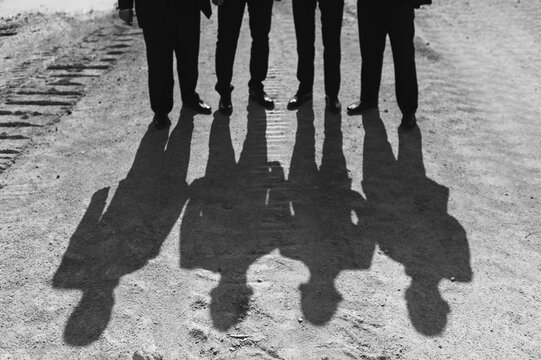 Shadow of a group of faceless people in black suits on a bright sunny day on the sand.